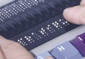 Primo piano delle celle di un display braille con i punti sollevati, mentre un dito le legge