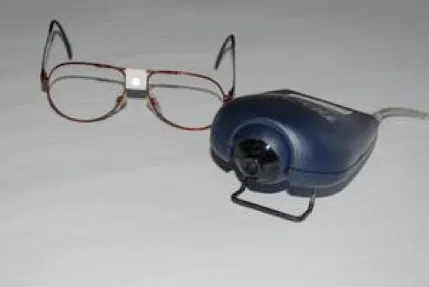 Un paio di occhiali con un piccolo bersaglio riflettente al centro, accanto a una telecamera a infrarossi